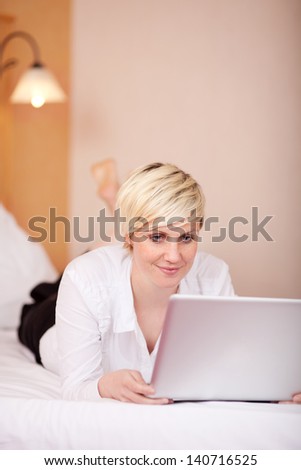 Portrait of reading businesswoman with laptop while lying on bed in hotel room