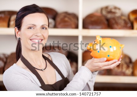 Smiling woman baker in apron holding a golden piggybank