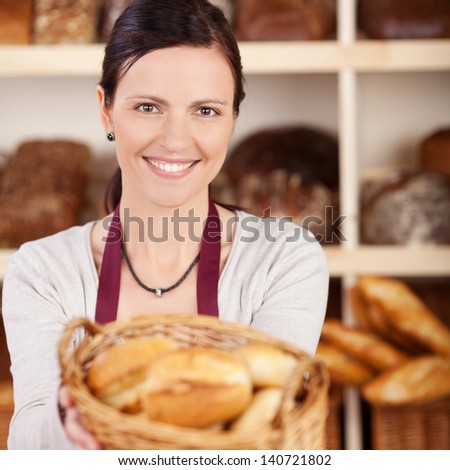Beautiful female bakery worker with a charming friendly smile offering a basket of assorted bread to the viewer