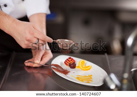 Closeup of chef\'s hand sieving coco powder in plate at commercial kitchen counter