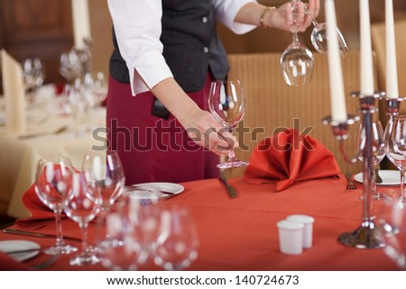 Midsection Of Waitress Arranging Wineglasses On Table In Restaurant