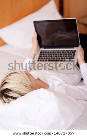 Young businesswoman using laptop while lying on bed in house