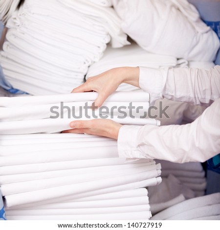 Closeup Of Female Housekeeper\'S Hands Stacking Sheet In Stock Room