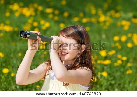 little girl looking through telescope on a green field