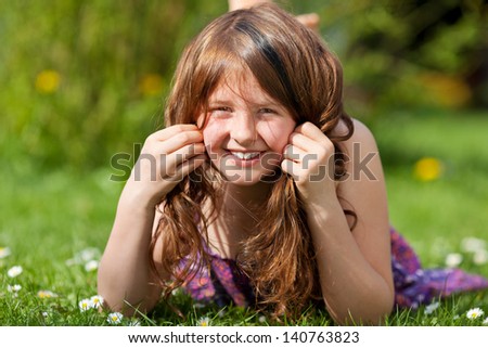 Portrait of young girl lying on grass while playing with hair in park