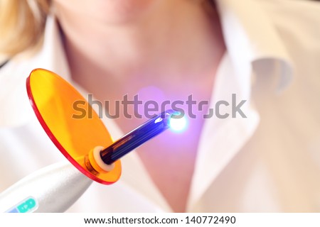 Close-up of a dentist holding a lit dental curing UV light