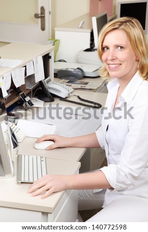 Female dentist assistant sitting at the computer behind the reception counter