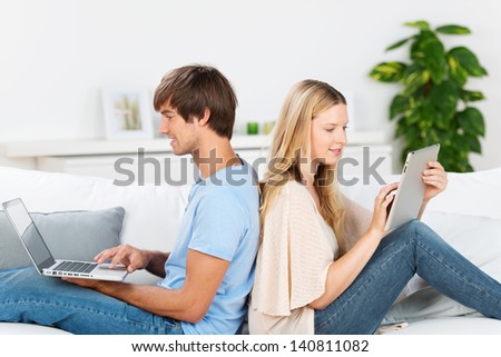 Couple Sitting On Sofa Working With Laptop And Tablet