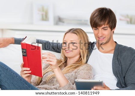 couple lying on the sofa reading book and tablet