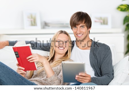 couple reading book and ebook, sitting on the sofa