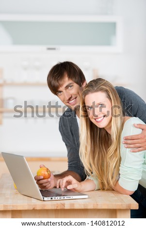 smiling couple standing with laptop in the kitchen