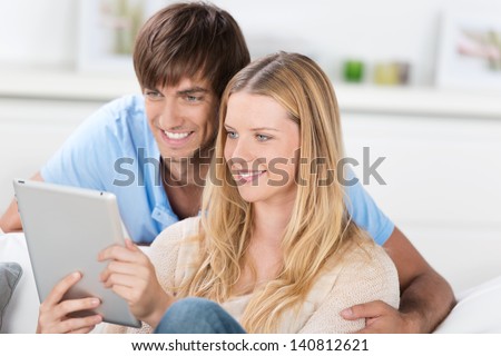 couple sitting on the sofa, reading together on tablet
