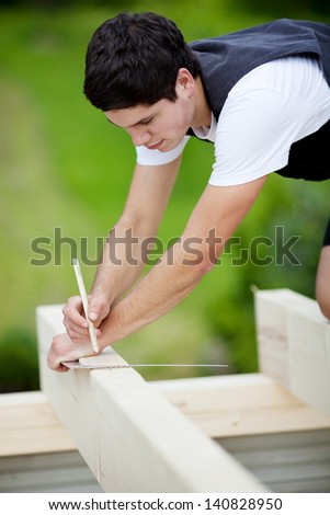 Carpenter making markings on a roof beam using a pencil and a steel square