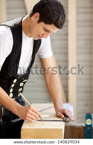 Young construction worker marks a piece of wood