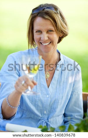 Portrait of happy mature woman holding white wine in lawn