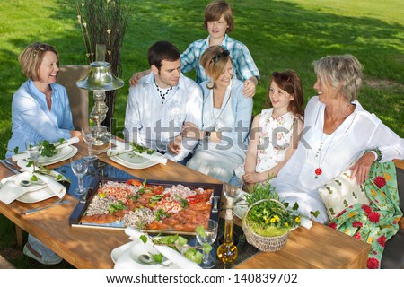 Happy Family Sitting Together At Dining Table In The Garden