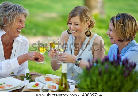 Happy Mother And Daughters Toasting White Wine At Dining Table In Lawn