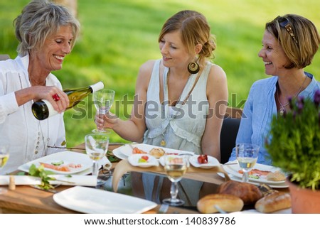 Senior woman pouring wine in glass for daughter at dining table in lawn