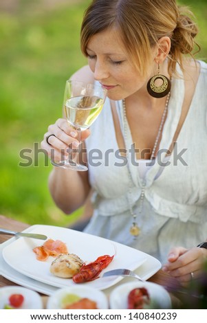 Young woman with food plate having white wine in crayfish party at lawn