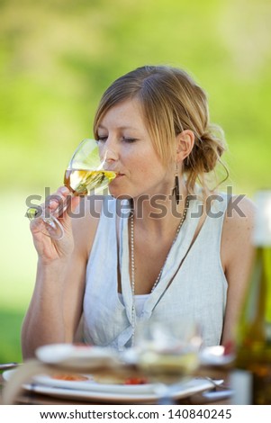 Young woman drinking white wine at dining table in lawn