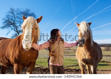 Pretty young girl leading two palomino horses on the paddock on a sunny day