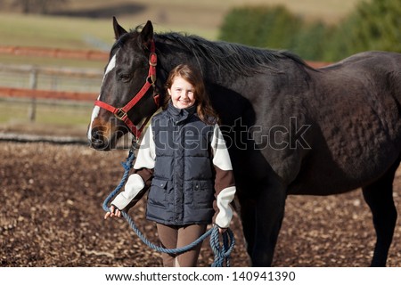 Smiling young girl leading her dark bay horse in the paddock