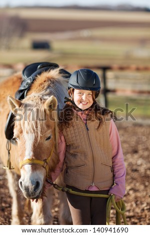 Young girl leading horse to stable and wearing a modern horse riding helmet