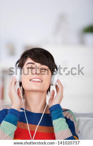 Young woman enjoying her music sitting with her eyes closed and head tilted back listening to her headphones