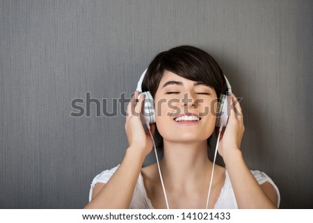 Head and shoulders studio portrait of a young woman listening to music on a set of headphones standing with her eyes closed in bliss