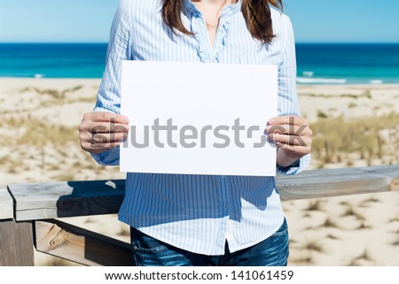 midsection of woman showing white paper standing by the beach