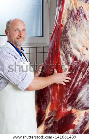 Middle-aged butcher near a hanging cow carcass inside a butchery