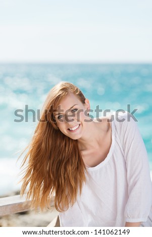 Vivacious young redhead woman at the seaside backlit by the sun dancing off the sea