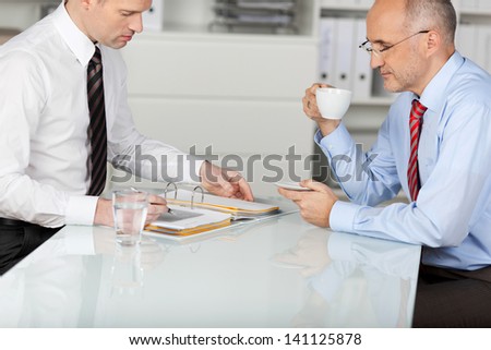 Two employees having a coffee while searching something in binder