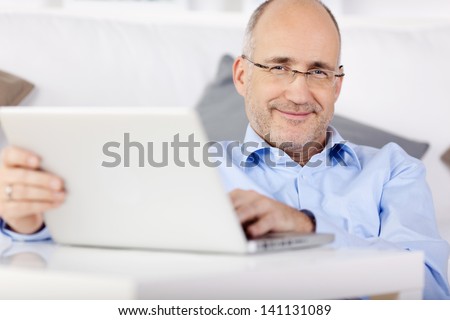 Smiling man holding laptop while leaning on the couch at home