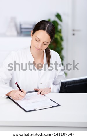Mid adult receptionist signing prescription on clipboard at hospital reception