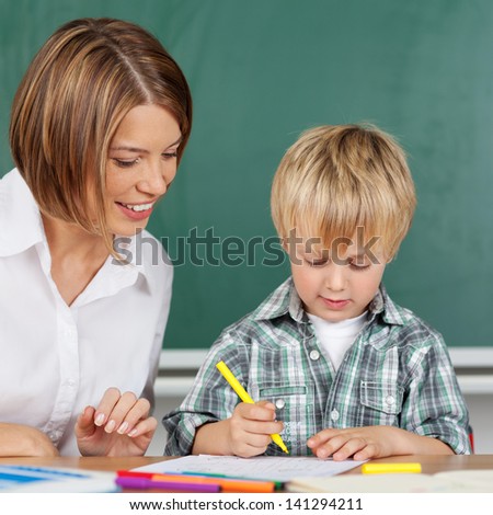 Little boy is coloring with teacher in kindergarten