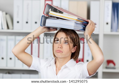 Young businesswoman or office worker wearing a bright white blouse holding a stack of file folders over her head