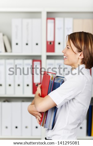 Smiling businesswoman or office worker holding a stack of file folders in office