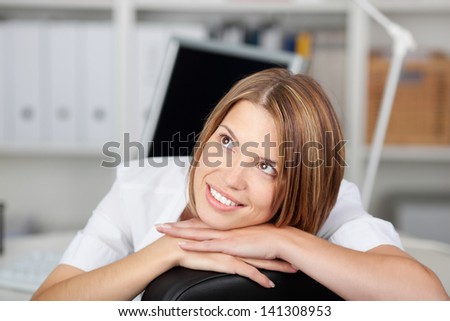 Thoughtful woman resting her head on her hands as she sits in her chair at the office staring up into the air with a smile