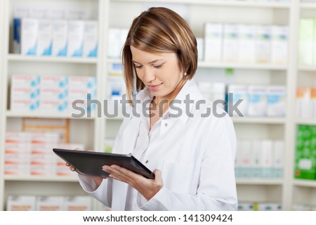 Pharmacist Working With A Tablet-Pc In The Pharmacy Holding It In Her Hand While Reading Information