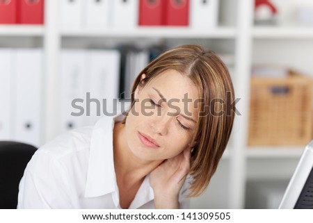 Woman with a stiff painful neck rubbing the back of her head with her hand and grimacing in pain