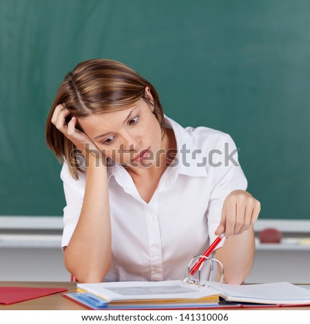 Depressed young female student sitting staring at her notes with her head on her hand in front of a blackboard