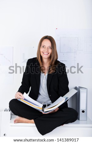 Full length portrait of mid adult businesswoman with binder sitting on counter at office