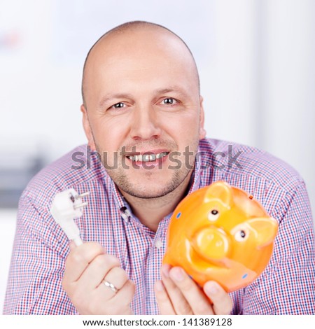 Portrait of mature businessman holding piggybank and electric plug in office