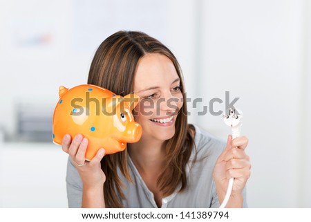 Portrait of happy mid adult businesswoman with electric plug and piggy bank in office