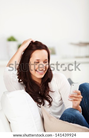 Smiling woman reading a message on her mobile while sitting relaxing curled up on a sofa