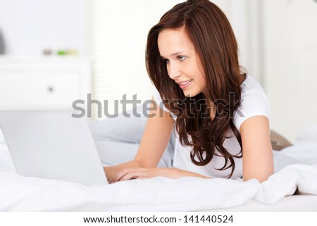 Beautiful brunette woman searching on her laptop in bed