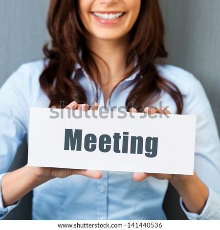 Smiling woman showing white card with meeting word in a close up shot