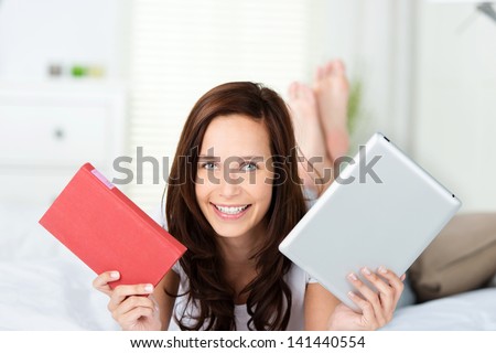 Smiling happy young woman holds up a book and a tablet-pc with an e-book as she tries to decide which is the best format