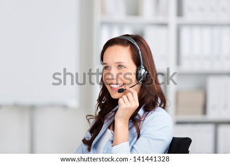 Smiling friendly woman wearing a headset sitting in an office, conceptual of customer support, receptionist or a call centre operator